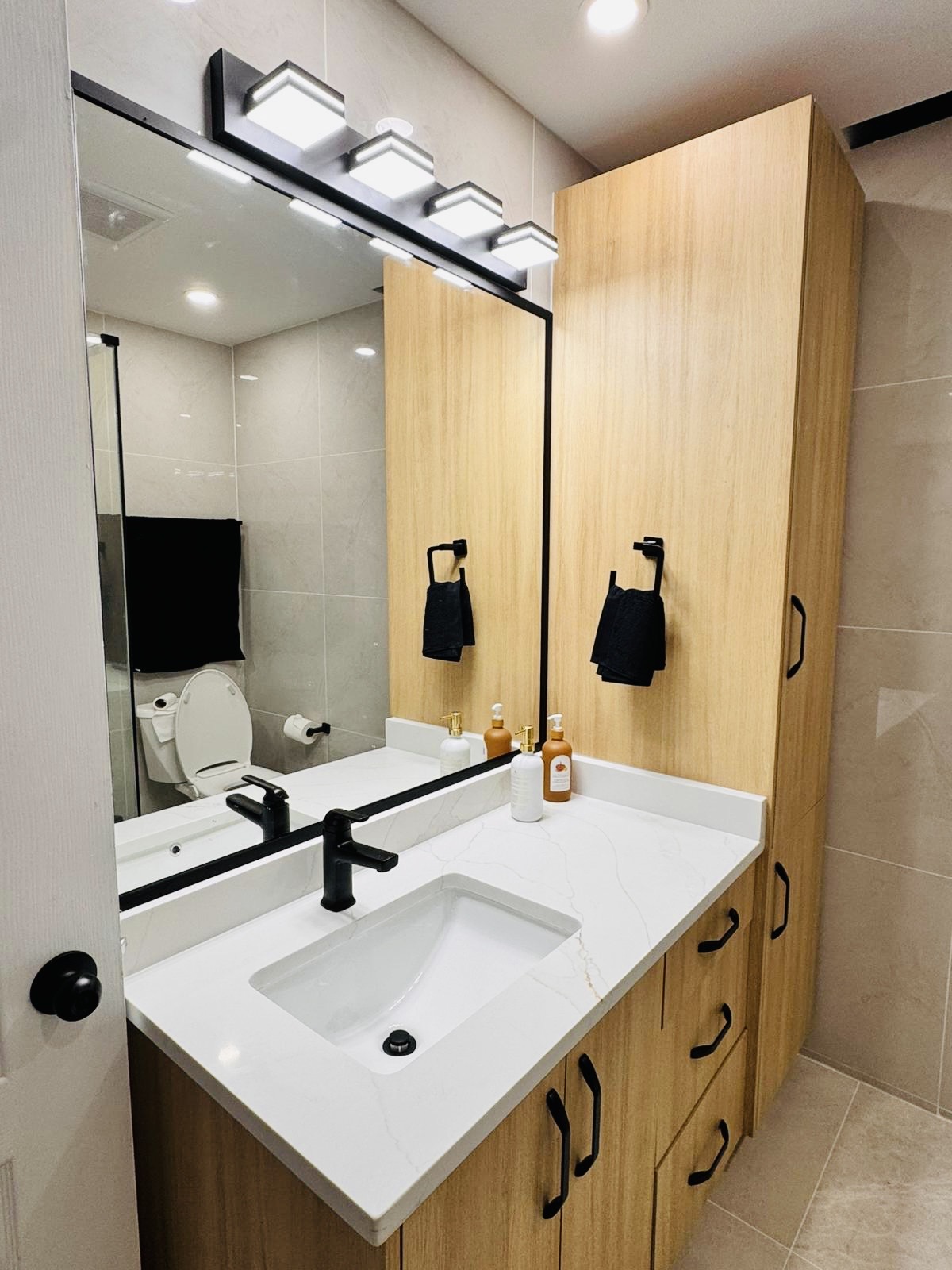 Timber vanity with black tapware under a backlit mirror